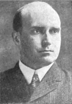 Mann im mittleren Alter von vorne und leicht nach rechts schauend um im grauen Anzug und weißem Hemd mit dunkler Krawatte in schwarzweiß ab Schulterblatt.