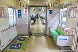 Innenraum eines durchgängigen Zuges der Baureihe 2000 der U-Bahn Fukuoka mit Mehrzweckfläche für Rollstühle und Kinderwagen und Vorrangsitzen