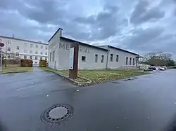 Das graue, flache Werkstattgebäude mit dem Alten Zuchthaus im Hintergrund.