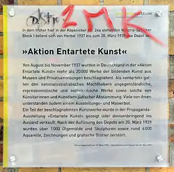 Farbfotografie von einer Tafel an einer Hauswand mit dem Titel „Aktion Entartete Kunst“. Das Aktive Museum Berlin erläutert das Depot mit entarteter Kunst aus den Jahren 1937 bis 1939.
