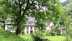 Ehemalige historische Mühle am Ende eines Bachtals umgeben von Bäumen und Wiesen.