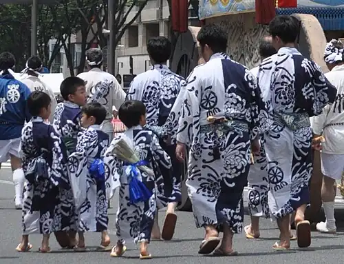 Erwachsene und Kinder in identischen Yukata beim Gion-Matsuri. Die Yukata der Kinder haben dieselbe Größe wie die der Erwachsenen, wurden aber mit Hilfe von Falten angepasst.