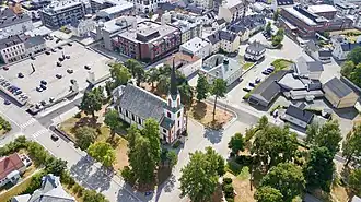 Luftbild mit einer Kirche im Zentrum, davor Grünfläche, dahinter ein Parkplatz und der Rest umgeben von mehrstöckiger, städtischer Bebauung