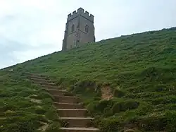 Der Turm einer Kirchenruine auf einem Hügel aus der Froschperspektive fotografiert. Vom Fuß des Hügels führt eine Treppe zum Turm.