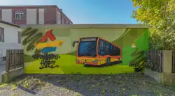 Das Foto zeigt die Ansicht eines Stromhäuschens mit einem Graffito, das einen Hofer Stadtbus und Text und Textlogo der Stadtwerke Hof zeigt