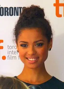 Gugu Mbatha-Raw steht vor einer weißen Wand mit der grauen Aufschrift toronto international film festival. Weiter oben steht das Wort Toronto in schwarzen Buchstaben sowie ein weiteres, abgeschnittenes Wort in orangen Buchstaben. Mbatha-Raw trägt ein dunkelblaues Oberteil, je einen goldfarbenen Ohrstecker in jedem Ohr sowie ihre schwarzen Haare als Hochsteckfrisur. Vor ihr sind der Kopf und das Mikrofon eines Reporters teilweise zu sehen.
