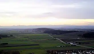 Heisteig von Nordosten (bewaldeter Höhenrücken in Bildmitte), im Hintergrund die Alpen