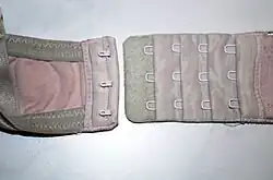 Dreifacher Hakenverschluss an einem Büstenhalter, durch die vier mal drei Ösen in vier Größen verstellbar.