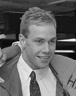 Dieses Schwarzweißfoto ist ein Ausschnitt aus einem Foto von Hans Kroes mit einigen Fans beim Abflug zu den Olympischen Spielen 1988. Kroes trägt einen Anzug sowie Hemd und Krawatte.