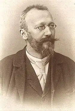 Hans Semper mit kurzen Haaren, Vollbart, kleiner runder Brille und in dunklem Anzug