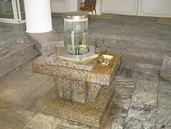 Steinsockel mit Wasserhahn und mit Wasser gefüllter Glassäule