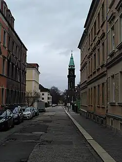 Gerade Straßenabschnitt ohne Fahrbahnmarkierung, links: Autos, rechts Gehweg, rechts hinten: Turm der Lutherkirche
