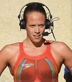 Hilary Caldwell nach einem Sieg im roten Badeanzug mit einem Headset auf dem Kopf. Am rechten Bildrand ist ein Oberarm-Tattoo erkennbar.