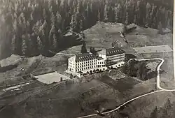 Die Luftaufnahme zeigt das Hochalpine Töchterinstitut Fetan um 1930 mit den beiden Tennisplätzen links vom Gebäude, den beiden Pavillons sowie dem institutseigenen Kräutergarten unterhalb des Gebäudes