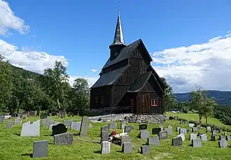 Foto einer hölzernen Stabkirche mit Turm, im Vordergrund ein Friedhof