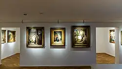 Ein Museumsraum mit Genregemälden und zwei durchgängen zu weiteren Räumen