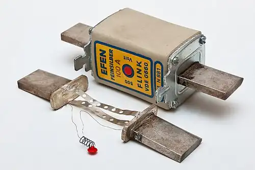 NH-Sicherung 100&nbsp;A mit Mittenkennmelder (rot). An der zerlegten Sicherung sind der Schmelzleiter und der Auslösedraht des Kennmelders zu sehen.