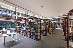 Innenansicht des TIB-Standortes Sozialwissenschaften mit hohen Bücherregalen, Leseplätzen und großen Fenstern.