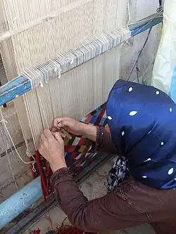 Teppichknüpferin an einem aufrechten Webstuhl vom „Täbris“-Typ