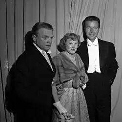 Drei vor einem Vorhang stehende Personen bei der Oscarverleihung 1950 von vorn in schwarzweiß.