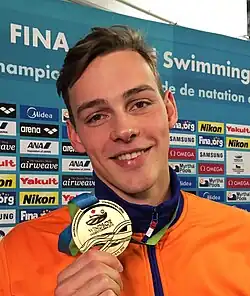 Jesse Puts trägt eine orangefarbene Trainingsjacke und steht vor einer Werbetafel.