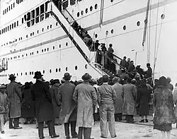 Zahlreiche Menschen mit Gepäck verlassen ein mehrstöckiges weißes Schiff