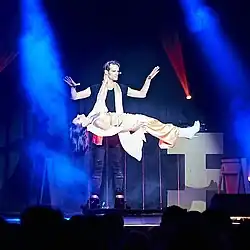 Zauberer Julius Frack steht auf der Bühne, vor ihm schwebt seine Partnerin in horizontaler Lage auf roten Laserstrahlen