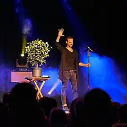 Zauberer Julius Frack steht auf der Bühne und präsentiert den Zaubertrick mit seinem magischen Orangenbaum