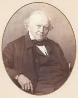 Das Bild zeigt ein rundes Porträt eines alten, schwarz gekleideten Mannes.