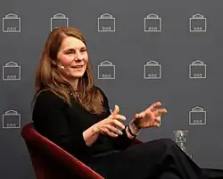 "Kerstin Kohlenberg im Halbprofil, sprechend, lächelnd und gestikulierend, auf einer Bühne des Amerikahauses München