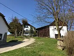 Von l.&nbsp;n.&nbsp;r.: Nr. 14 Lehrerhaus. Holzkreuz anstelle Kirchturm. Nr. 15 Mesnerhaus. Totenhäusl, Gruft der Herrschaft Clam