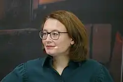 Porträtfoto einer Frau, die freundlich nach rechts blickt. Man sieht das Mikrofon eines Headsets vor ihrem Mund.