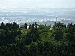 Blick vom Aussichtsturm des Großen Feldbergs zum Gipfel des Kleinen Feldbergs, dahinter der Fernmeldeturm auf dem Atzelberg und der Ort Bremthal sowie am Horizont Wiesbaden