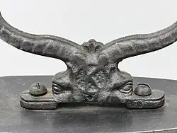 Delphinköpfe an der Unterseite der Bügel eines Kohlebügeleisens
