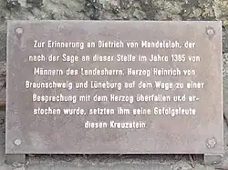 Tafelinschrift: Zur Erinnerung an Dietrich von Mandelsloh, der nach der Sage an dieser Stelle im Jahre 1385 von Männern des Landesherrn, Herzog Heinrich von Braunschweig und Lüneburg auf dem Wege zu einer Besprechung mit dem Herzog überfallen und er- stochen wurde, setzten ihm seine Gefolgsleute diesen Kreuzstein.