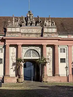 Historisches Gebäude mit Tor, auf dem sich die Skulptur einer Quadriga mit der Skulptur Johann Georg Pfunds befindet.