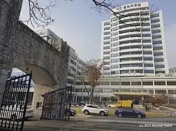 Das Bild zeigt ein weißes Hochhaus und ein Steintor mit geöffneten Türen