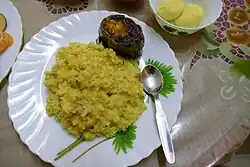 Teller mit einer großen Portion gelbem Khichuri, einem Stück Aubergine und einem kleinen Löffel
