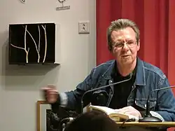 Siegfried Völlger an einem Tisch sitzend mit aufgeschlagenem Buch, spricht in ein Mikrofon