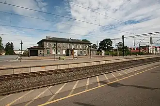 Foto eines Bahnhofsgebäudes mit Schienen im Vordergrund
