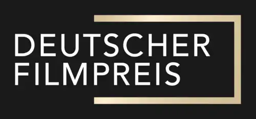 Das Bild zeigt das Logo des Deutschen Filmpreises. Es ist auf einem schwarzen Hintergrund dargestellt, was die anderen Elemente des Logos betont. Im Zentrum des Logos befindet sich der Schriftzug „DEUTSCHER FILMPREIS“ in Großbuchstaben und in einer modernen, serifenlosen Schriftart. Die Buchstaben sind weiß und stehen klar im Kontrast zum dunklen Hintergrund. Der Text wird von einem goldenen Rahmen eingefasst, der an der oberen und rechten Seite des Logos sichtbar ist. Dieser Rahmen verleiht dem Logo eine elegante und hochwertige Wirkung, die die Bedeutung des Deutschen Filmpreises als renommierte Auszeichnung in der deutschen Filmindustrie unterstreicht.