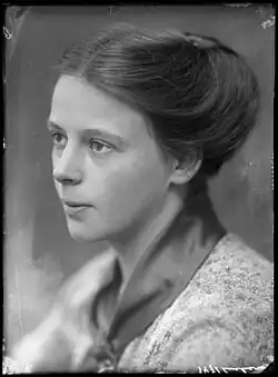 Schwarz-Weiß-Porträt einer ernst blickenden, jungen Frau im Profil mit kleingemustertem Oberteil und hochgesteckten Haaren.