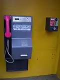 Münztelefonapparat mit Tastenfeld und Telefonhörer in der Telekom-Farbe Magenta, sowie einem Notrufhebel