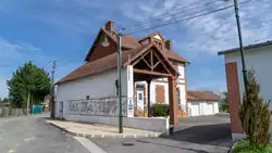 Weißes Hauptgebäude am Straßenrand mit rotem Giebeldach mit hinten gelegenen Garagen und Garagenhof in Blickrichtung des neben den Garagen befindlichen Eingangs.