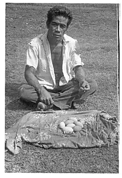 Schwarz-Weiß-Photographie eines Tonganers mit acht länglichen Eiern des Großfußhuhns auf einem Tuch