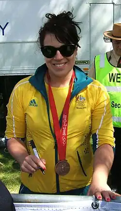 Mia Santoromito trägt eine gelbe Trainingsjacke mit grünem Kragen. An einem roten Band um ihren Hals ist die Bronzemedaille befestigt.