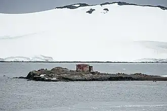 Die kleine Insel D’Hainaut im Mikkelsen Harbor, mit der argentinischen Schutzhütte und zahlreichen Eselspinguinen, und im Hintergrund die vergletscherte Steilküste der Trinity-Insel