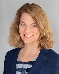 Miriam Holstein ist im Porträt lächelnd in die Kamera blickend zu sehen. Sie hat leicht gewelltes, blondes schulterlanges Haar.