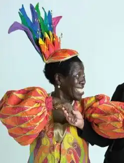 etwa 75jährige Frau mit strahlendem Lächeln in Tanzpose in einem bunten Kostüm