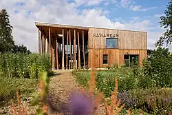 Ein Holzgebäude, welches mit NAWAREUM beschriftet ist. Im Vordergrund ist ein blühender Garten.